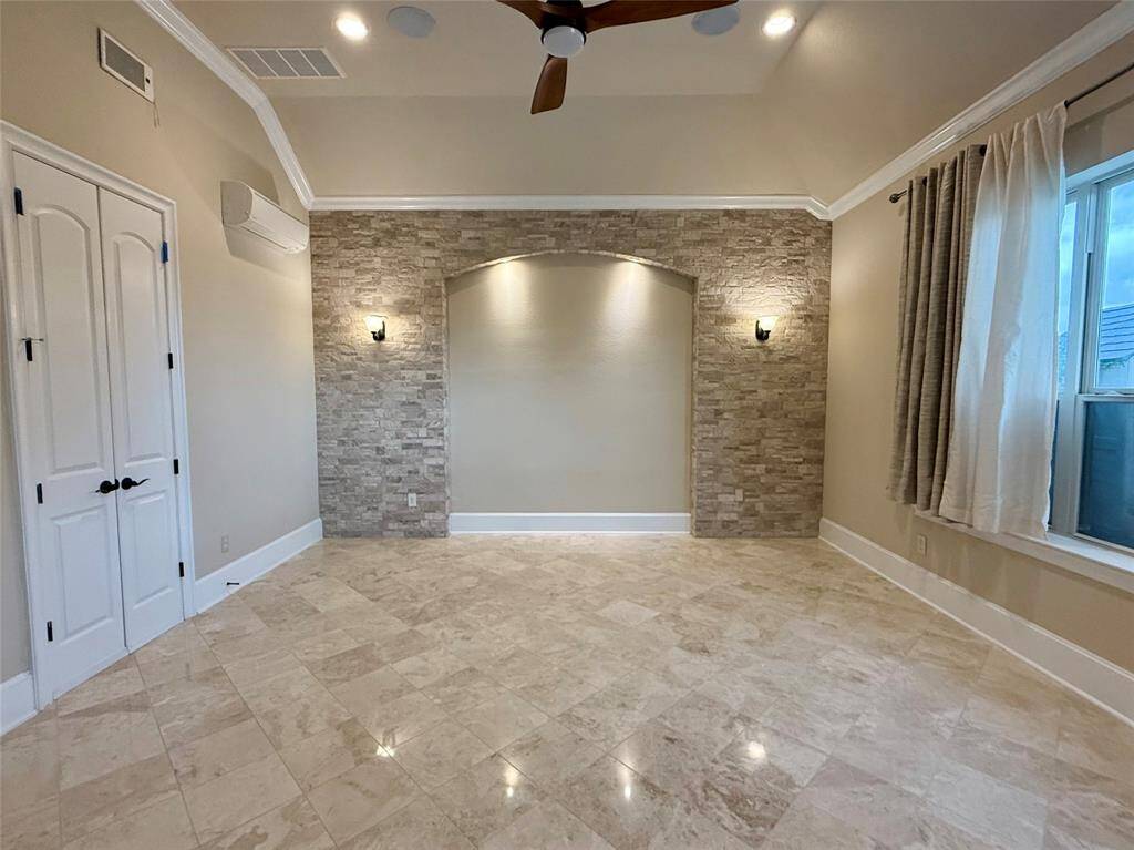 Spacious room featuring elegant stone accent walls, polished tile flooring, and ample natural light from large windows. The ceiling fan and wall sconces add a touch of modern comfort.