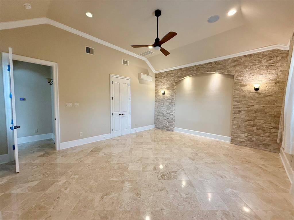 This spacious room features high ceilings, marble flooring, and a decorative stone accent wall. It has recessed lighting, a ceiling fan, and double doors, offering a modern and elegant touch.