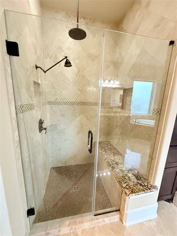 Main room with a modern, spacious shower with a glass enclosure, tiled walls, and a built-in granite bench. The shower includes a rainfall showerhead and elegant accent tiles for a touch of luxury.