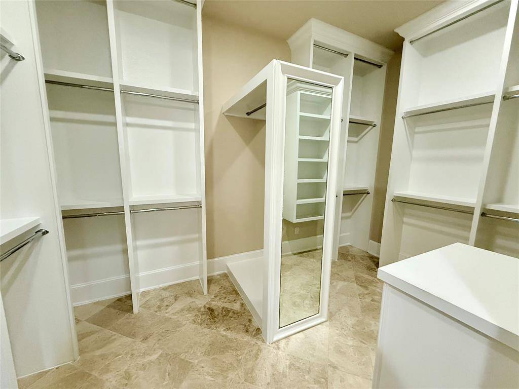 Spacious walk-in closet with ample shelving, hanging space, and a central island featuring a full-length mirror. Bright and organized for optimal storage.