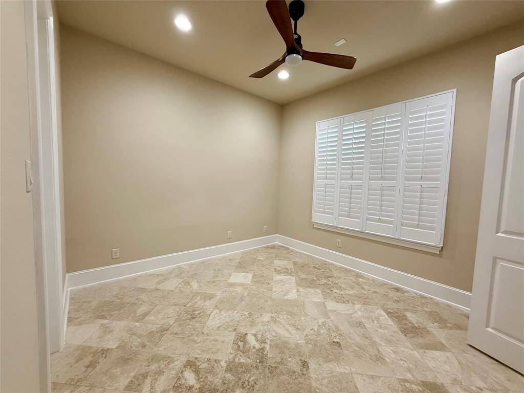 This room features neutral walls and tile flooring, with a ceiling fan and recessed lighting. It has a window with plantation shutters, providing a clean and modern look.