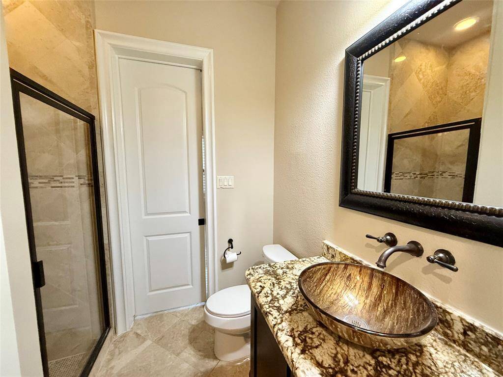 This bathroom features a modern design with a glass-enclosed shower, a vessel sink on a granite countertop, and a large framed mirror, creating a stylish and functional space.