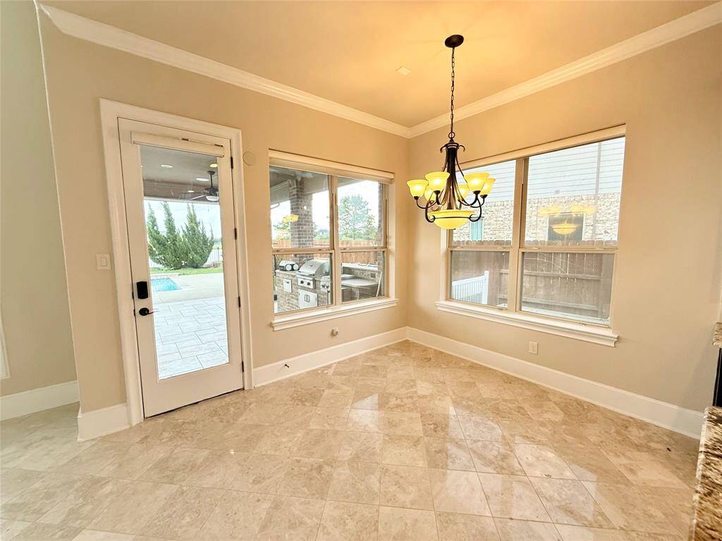 Bright breakfast area with large windows, a stylish chandelier, and tile flooring. It features a door leading to a patio with a built-in grill, perfect for indoor-outdoor entertaining.