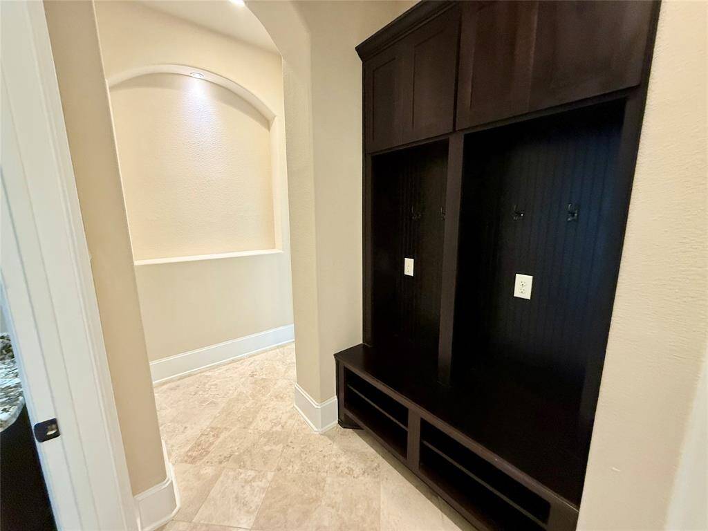 Hallway with tiled flooring and built-in dark wood storage units, ideal for coats and shoes. The space has a recessed archway with soft lighting, adding a touch of elegance.