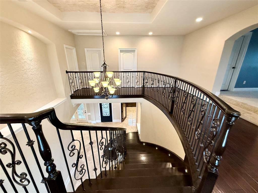 This elegant home features a grand curved staircase with dark wood steps and ornate wrought iron railings, highlighted by a stylish chandelier. The open space and high ceiling create a luxurious and inviting entryway.