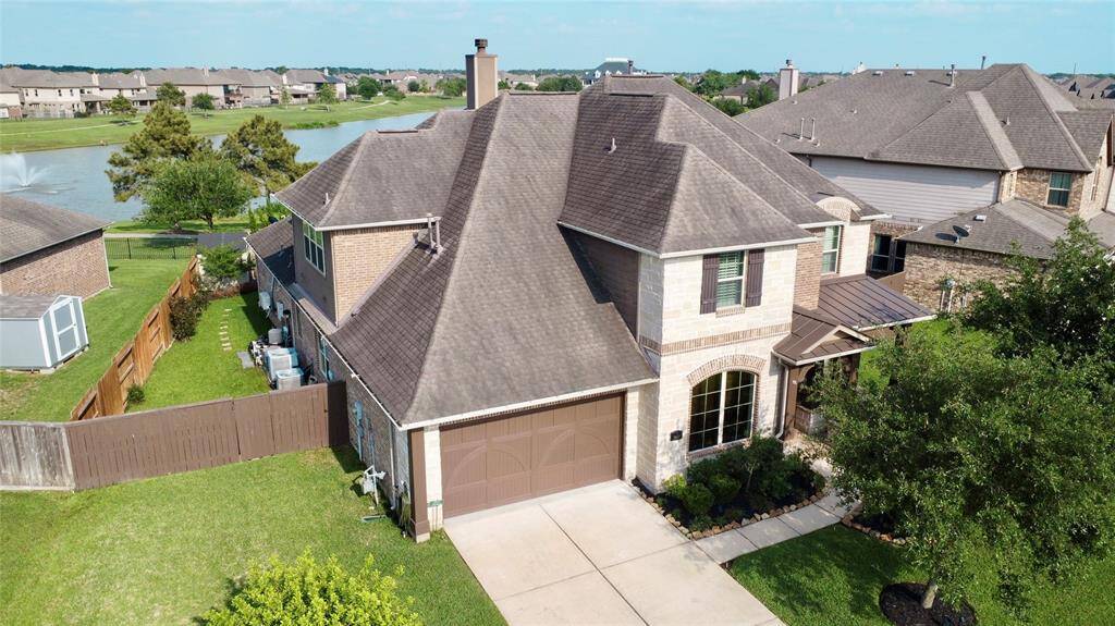 This two-story home features a brick exterior and a spacious two-car garage. It has a well-maintained front yard and a private fenced backyard. Located in a peaceful neighborhood, it offers a scenic view of a nearby lake with a fountain, enhancing its serene setting.