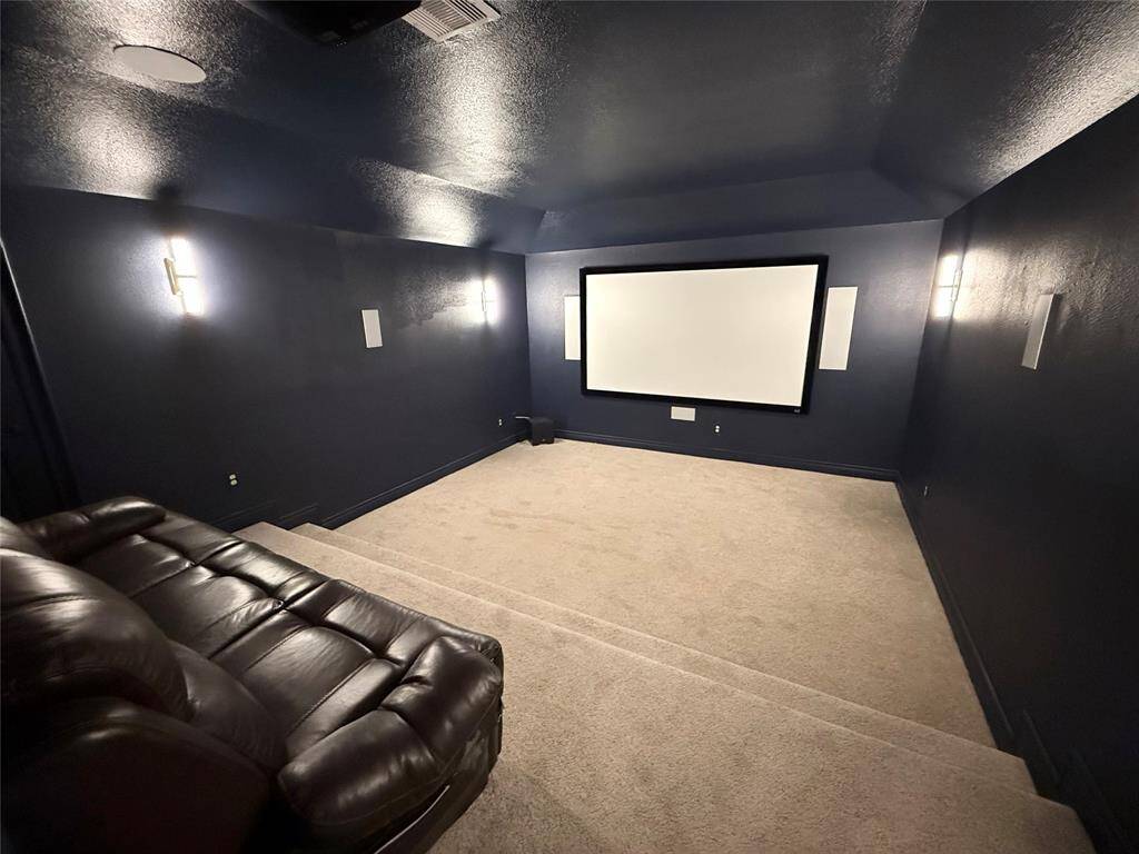 Cozy home theater room featuring dark walls, a large screen, plush carpeting, and comfortable tiered seating, creating an ideal space for movie nights.