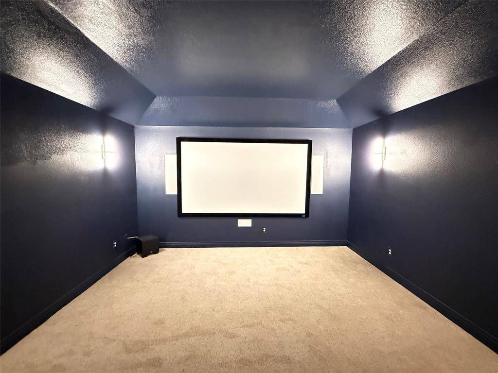 Modern home theater room with dark blue walls, a large screen, wall sconces for ambient lighting, and a carpeted floor, creating a cozy entertainment space.