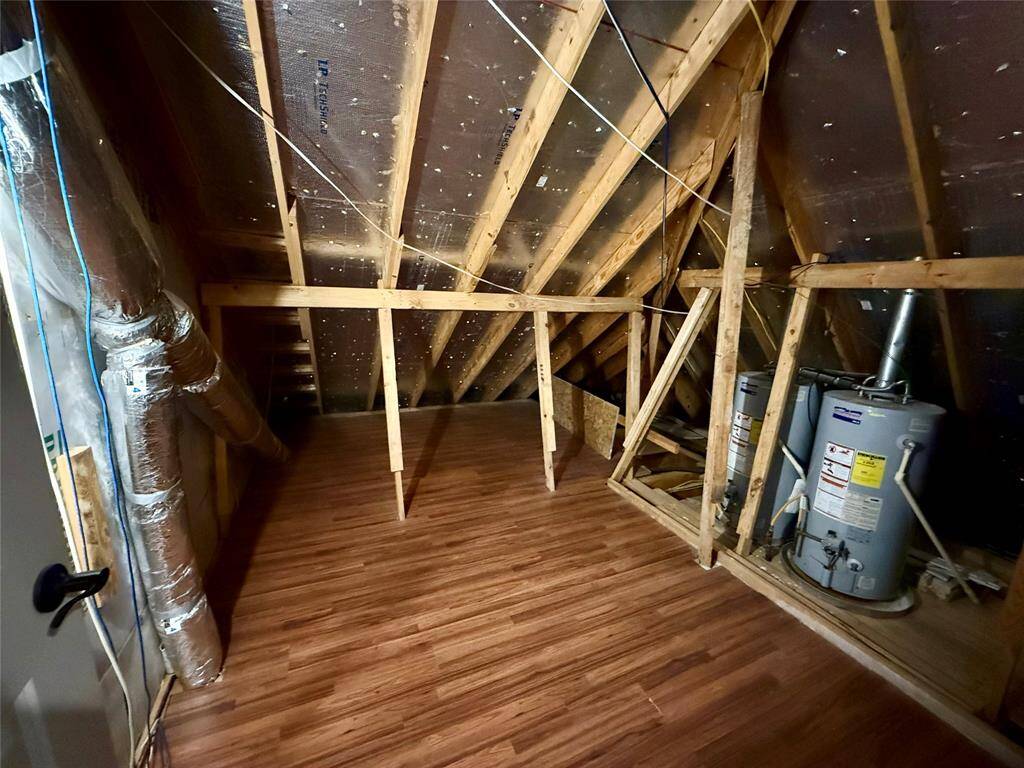 Attic space with a sloped ceiling, exposed wooden beams, and laminate flooring. It includes a water heater and ductwork, offering potential for storage or other uses.