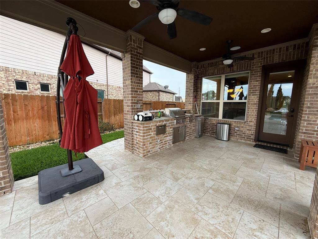 This outdoor patio features a covered space with ceiling fans, a built-in grill and countertop, and attractive brickwork. It's perfect for entertaining, with tiled flooring and a fenced yard offering privacy.