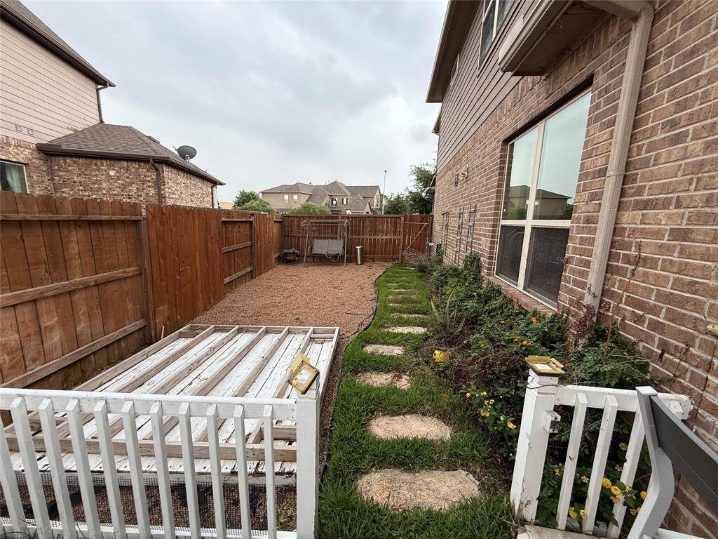This backyard features a cozy, fenced-in space with a gravel area perfect for seating. It includes a narrow garden bed with stepping stones and a small patio section adjacent to a brick exterior. Ideal for low-maintenance outdoor enjoyment.