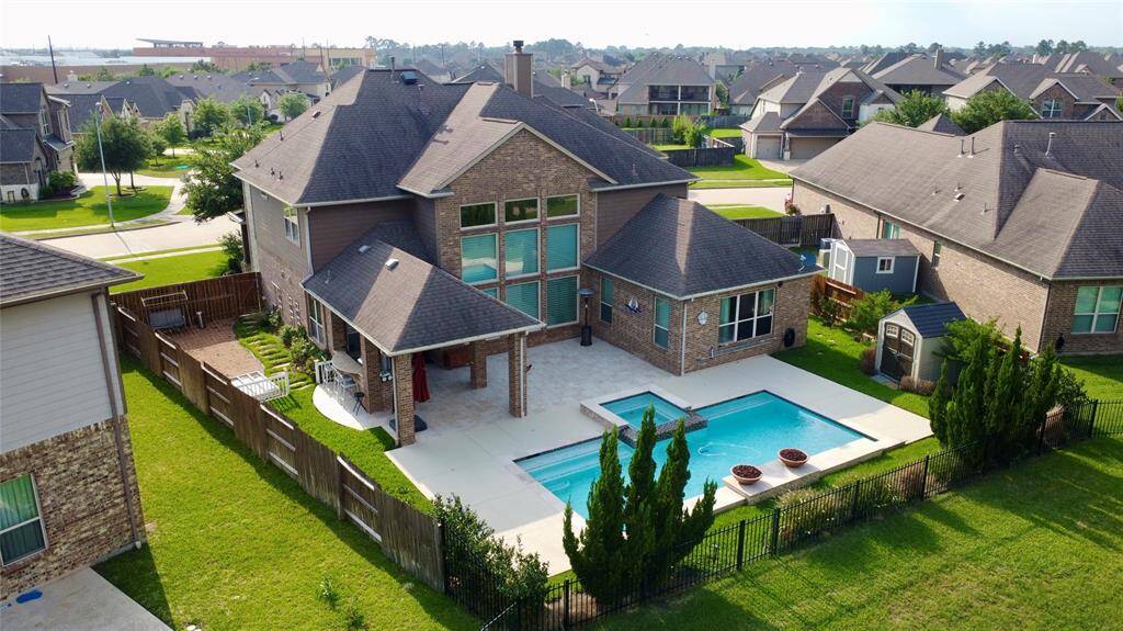 This spacious two-story home features a large backyard with a pool and patio area, perfect for entertaining. The house has a brick exterior and a mix of modern and classic design elements, situated in a suburban neighborhood.