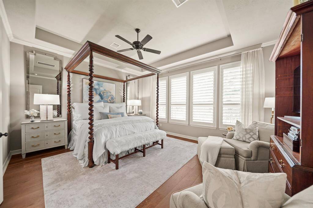 The peaceful primary suite is accented with a tray ceiling, crown molding, custom wood shutters and wood floors.