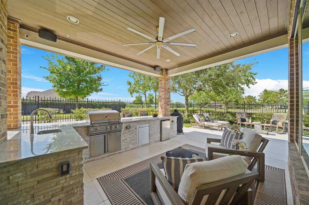 Outdoor living abounds with this beautiful outdoor kitchen offering travertine flooring, upgraded granite countertops, 30" gas grill, sink and refrigerator.  The large fan and outdoor speakers add to the ambience.