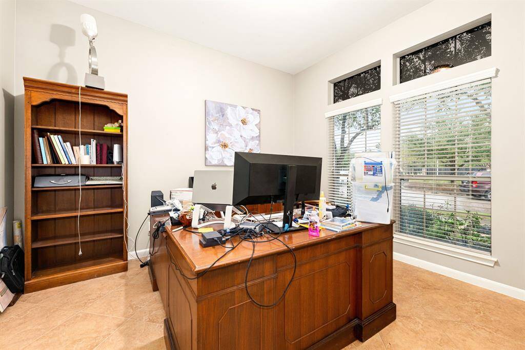 This versatile home office space features abundant natural light streaming in from large windows, perfect for productivity. The neutral tones and tile flooring provide a bright, comfortable atmosphere.