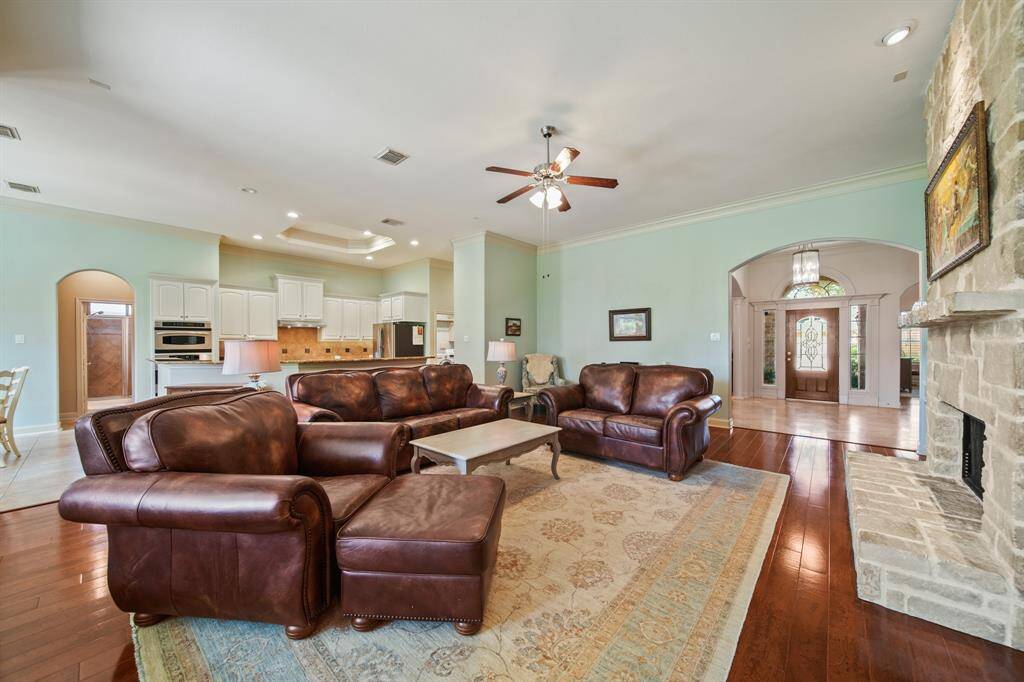 A spacious open-concept living area with high ceilings, featuring a cozy stone fireplace and elegant hardwood floors. The room flows into a modern kitchen with white cabinetry and stainless steel appliances, creating a warm and inviting atmosphere.
