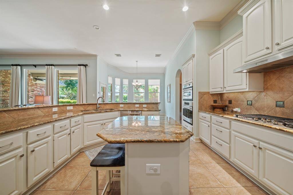 This spacious kitchen features granite countertops, ample cabinetry, and a central island. It includes a gas cooktop, oven and microwave, and large windows for natural light. The open layout connects seamlessly to the dining area, ideal for entertaining.