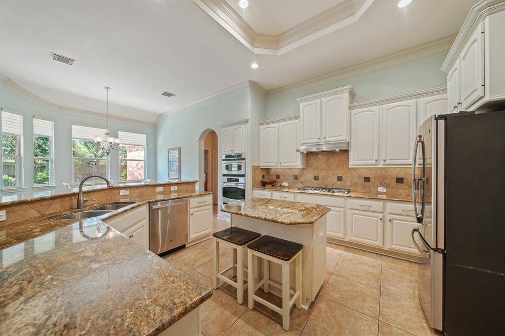 This spacious kitchen features elegant granite countertops, white cabinetry, stainless steel appliances, and a central island with seating. Large windows provide ample natural light, and the open layout is perfect for entertaining.