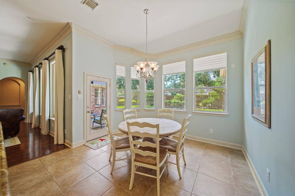Bright breakfast nook with large windows offering garden views. Features tile flooring and a chandelier. Adjacent to an open living area with hardwood floors.