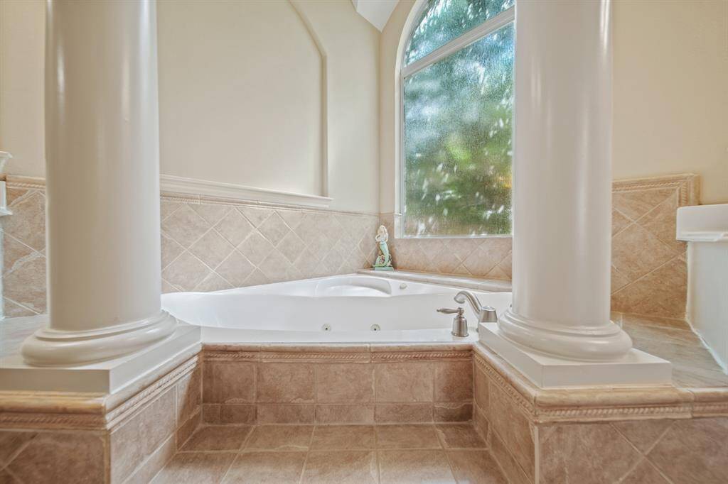 Luxurious bathroom featuring a deep soaking tub with elegant pillars, tiled surround, and a large frosted window for natural light and privacy.