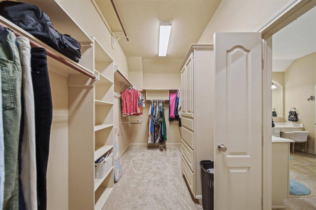 This spacious walk-in closet features ample shelving, hanging space, and built-in storage, leading to a bathroom area. Ideal for organizing clothes and accessories.