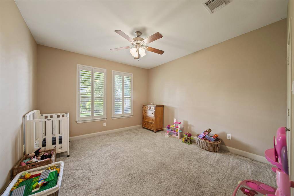 This bright, cozy room features neutral walls, carpeted flooring, and a ceiling fan. It is ideal for a child's bedroom or nursery. Large windows provide plenty of natural light.