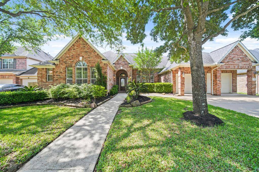 Welcome to your inviting home, featuring a charming pathway that leads through lush greenery to a beautiful brick facade.
