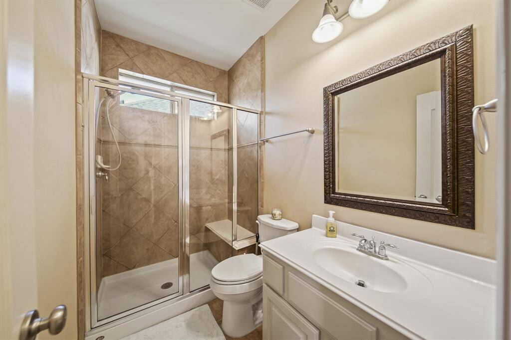 This bathroom features a modern glass-enclosed shower with tile walls, a sleek vanity with a polished sink, and a large framed mirror. The neutral color palette creates a warm and inviting atmosphere.