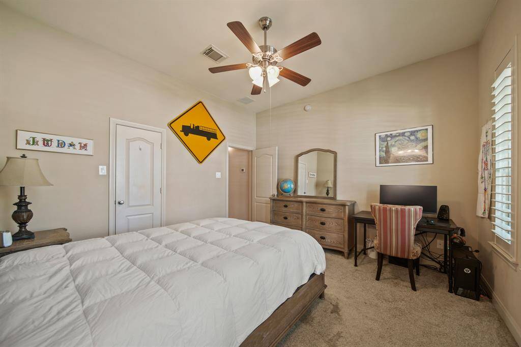 This cozy bedroom features ample natural light from a window with shutters, and a ceiling fan for comfort. Neutral tones create a relaxed atmosphere.