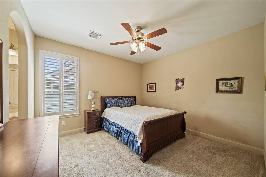 This cozy bedroom features a neutral color scheme, carpeted flooring, and a ceiling fan. It includes a window with plantation shutters, creating a warm and inviting atmosphere.
