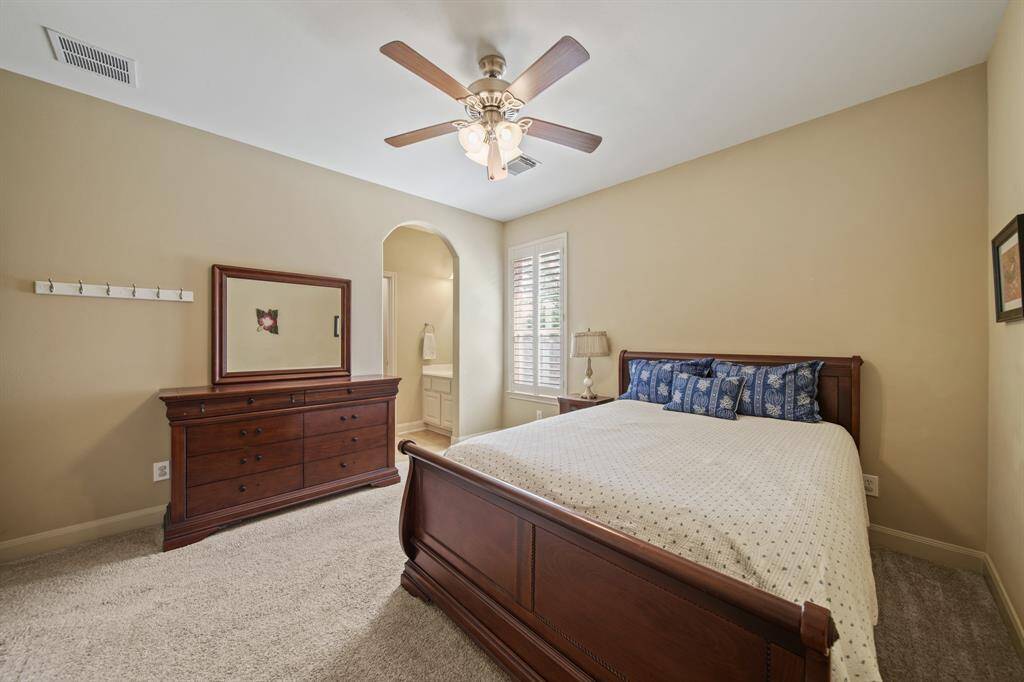 This cozy bedroom features neutral walls, a ceiling fan, and carpeted flooring. with a window letting in natural light. An open doorway leads to an adjoining jack and jill bathroom.