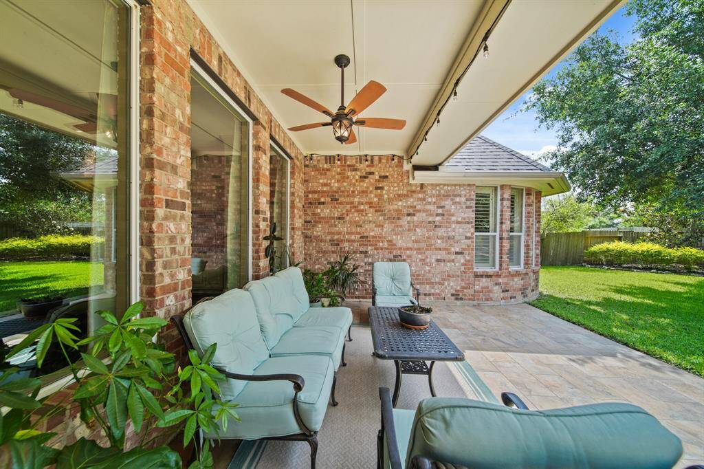 Charming patio with a brick exterior. Imagine comfy seating, and a ceiling fan. Overlooks a lush, green backyard, perfect for relaxing or entertaining.