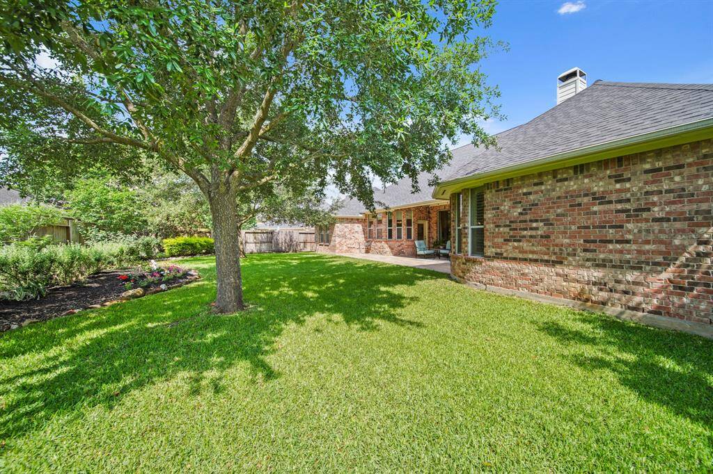 This photo showcases a spacious backyard with a lush green lawn, a mature tree providing shade, and a cozy patio area. The brick exterior of the house adds a classic touch, and the garden beds are well-maintained, offering a serene outdoor space.
