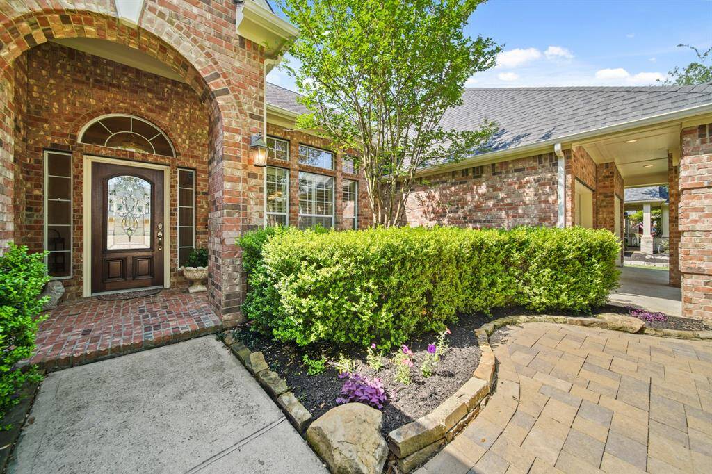 Charming brick exterior with an inviting arched entryway and decorative glass front door. The front yard features well-maintained landscaping, including lush greenery and a paved walkway. Perfect for creating a welcoming first impression.
