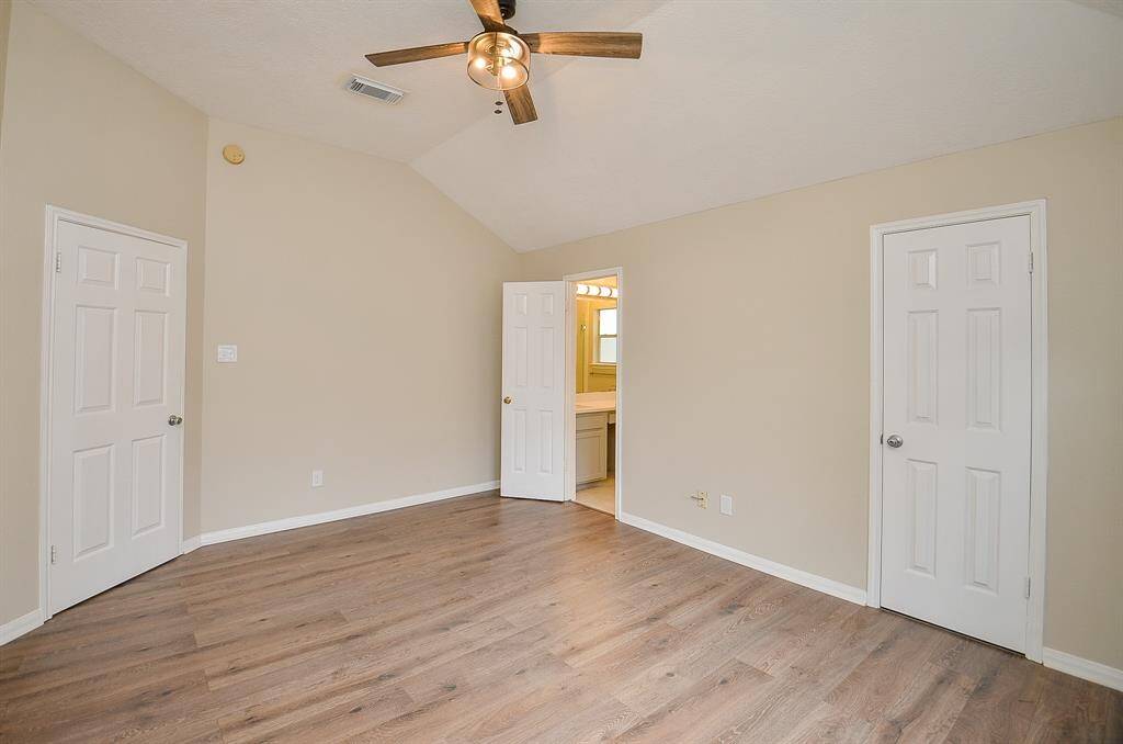This reverse view of the spacious primary bedroom with brand new flooring, neutral tones, and vaulted ceiling. It features a walk in closet, an en-suite bathroom, and a stylish ceiling fan for comfort.