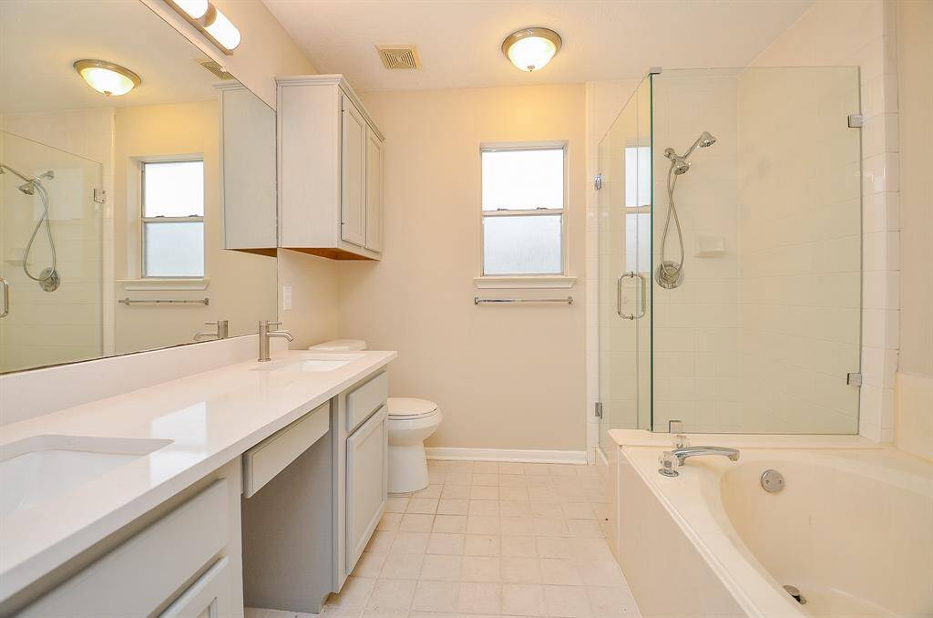 The primary bathroom has been recently updated, featuring a seamless glass shower surround, quartz countertops with double sinks, vanity space for your morning routine, and freshly painted modern grey cabinetry.