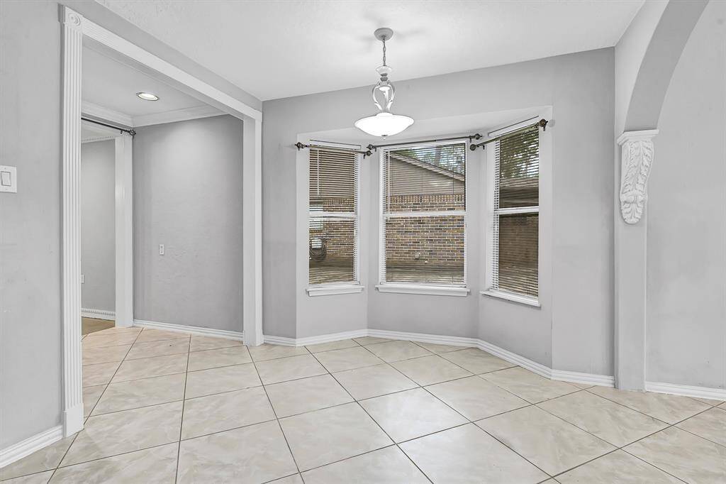 Bright dining area with large windows and neutral tile flooring, featuring soft gray walls and a modern light fixture. The space is open, inviting, and ready for personalization.