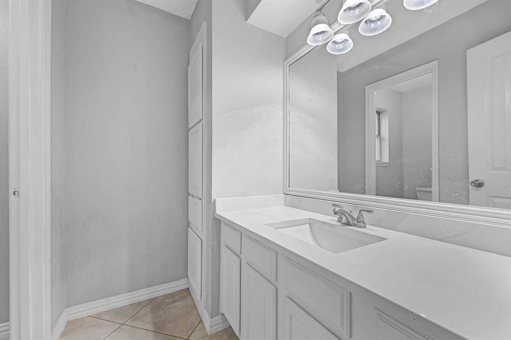 This bathroom features a sleek, modern design with a large mirror, ample counter space, white cabinetry, and neutral tile flooring, creating a bright and inviting atmosphere.