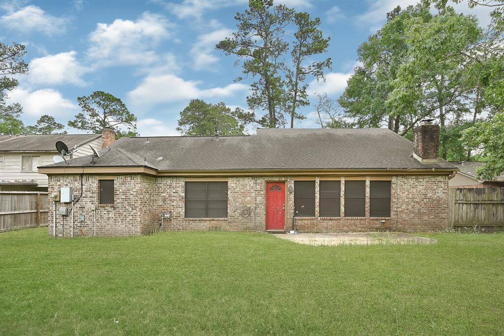 Charming brick home with a spacious backyard, featuring a red door and a patio area. Surrounded by mature trees, offering privacy and a serene atmosphere.