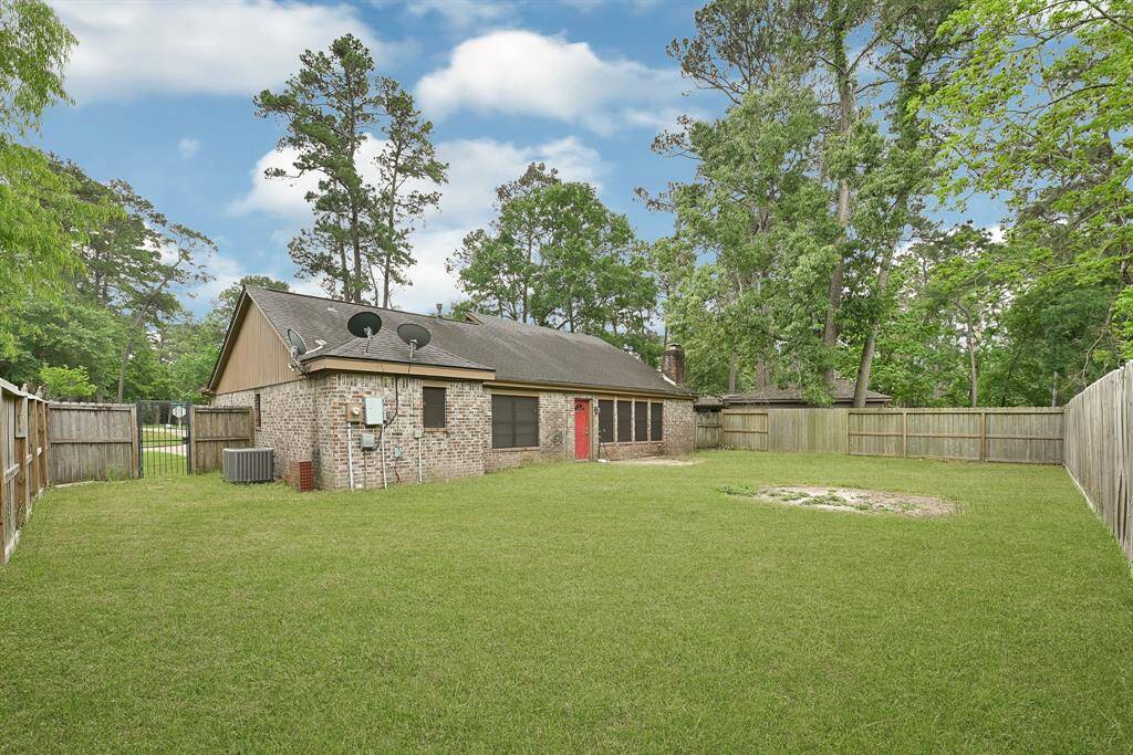 A spacious backyard with a lush lawn, surrounded by a wooden fence. The brick house features a sloped roof and is nestled among tall trees, offering privacy and a serene setting.