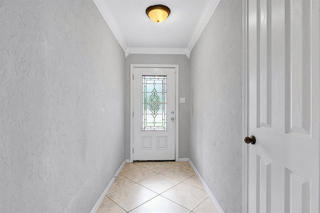 This entryway features a decorative glass front door, textured light gray walls, and neutral tile flooring, creating a welcoming and elegant first impression.