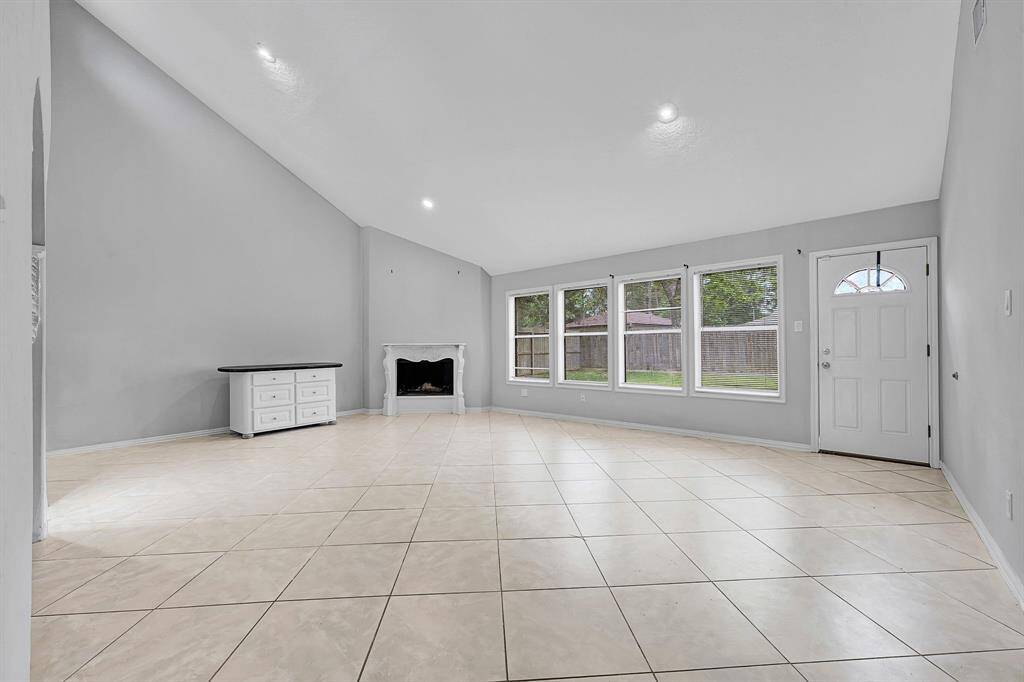 Bright and spacious living room with high ceilings, large windows for natural light, tiled floors, and a cozy fireplace.