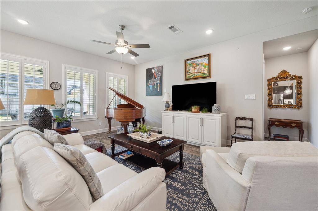 The open-concept living room features large windows with plantation shutters, recessed lighting, and an elegant ceiling fan, creating a cozy yet modern atmosphere.