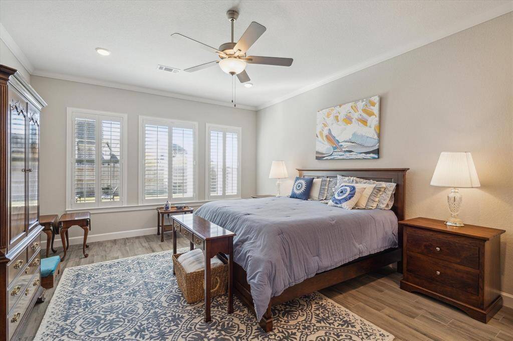 A serene primary suite with upgraded tile flooring, plantation shutters, and large windows offering natural light and backyard views creating a cozy and relaxing atmosphere.