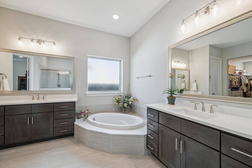 Alternate view of this well-appointed primary bathroom features ample counter space and elegant finishes throughout, including a luxurious corner bathtub with a frosted window, allowing natural light while maintaining privacy. Neutral tones and ample storage make this a serene and highly functional space.