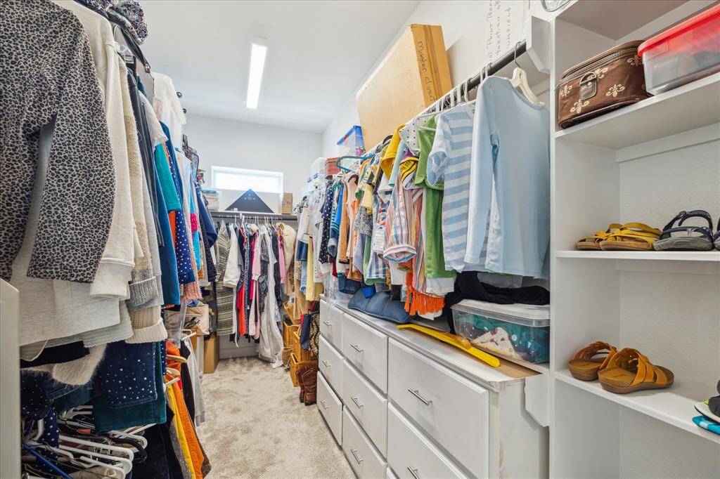 The primary suite boasts a large, well-organized walk-in closet with ample storage, featuring hanging rods on both sides for optimal organization. The space is well-lit with a modern light fixture and features a carpeted floor for comfort and functionality.