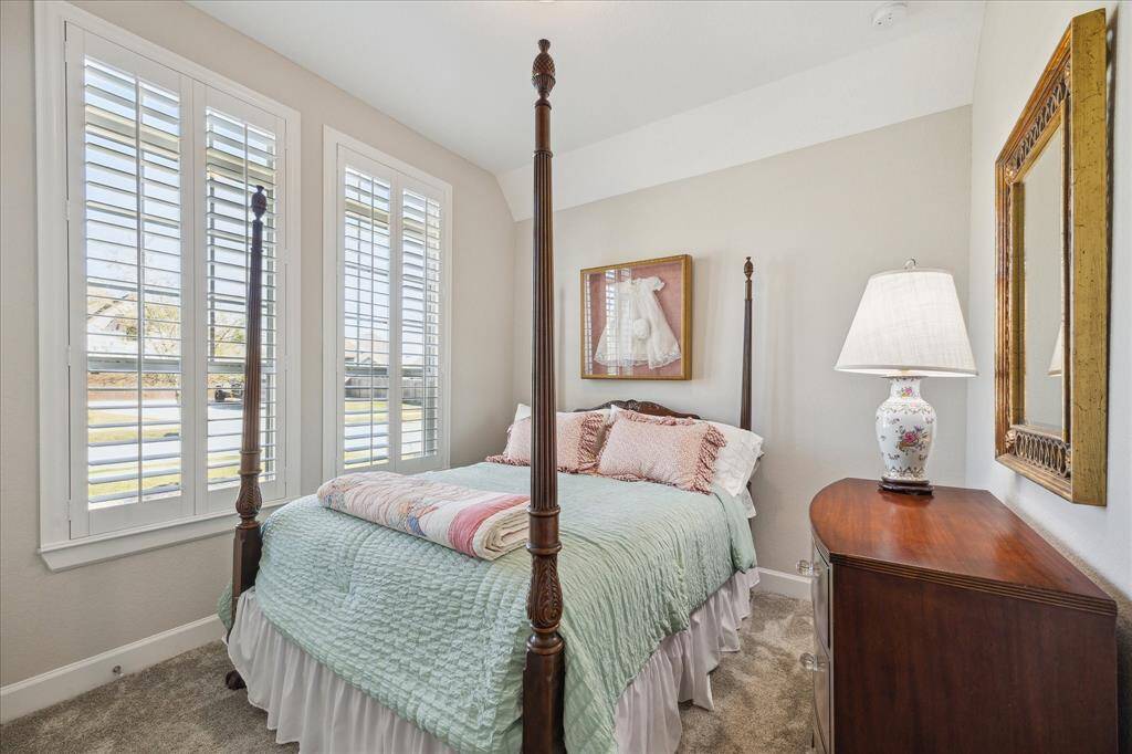 A charming secondary bedroom with plush carpet, plantation shutters, and plenty of natural light, perfect for guests or family members.