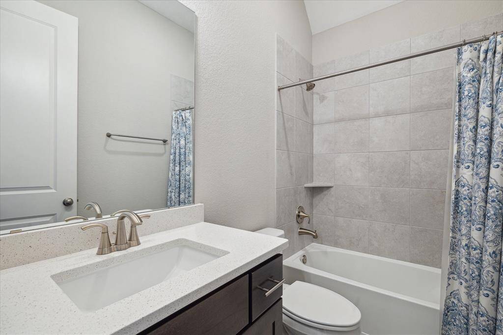The secondary bathroom carries through the same Kent Moore Groveland Grey Wolf cabinets and timeless Blanco Maple quartz countertops, complemented by ITSG Lakemont Gray 16x16 tile for the floor and shower, as well as elegant Moen nickel fixtures for a polished and cohesive look.