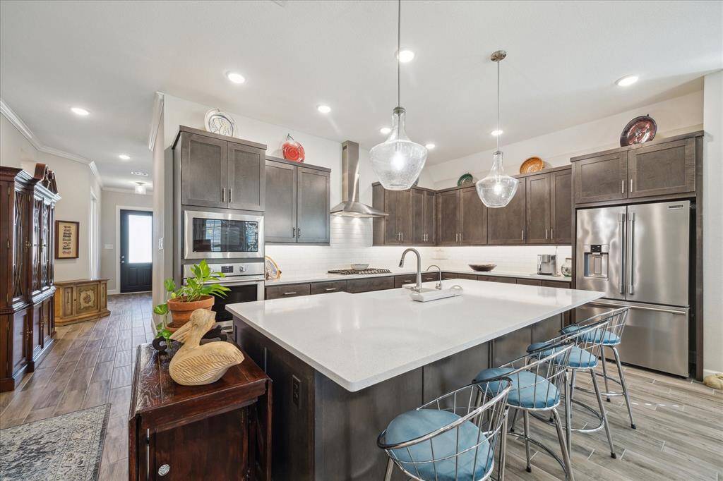 The kitchen is a showstopper with Kent Moore Groveland Grey Wolf cabinets, timeless Blanco Maple quartz countertops, a classic white subway tile backsplash, and stunning Kichler Everly island pendants. The open layout flows seamlessly into the living area with Norwood Oak 6x24 plank tile flooring, creating a stylish and functional space for entertaining.