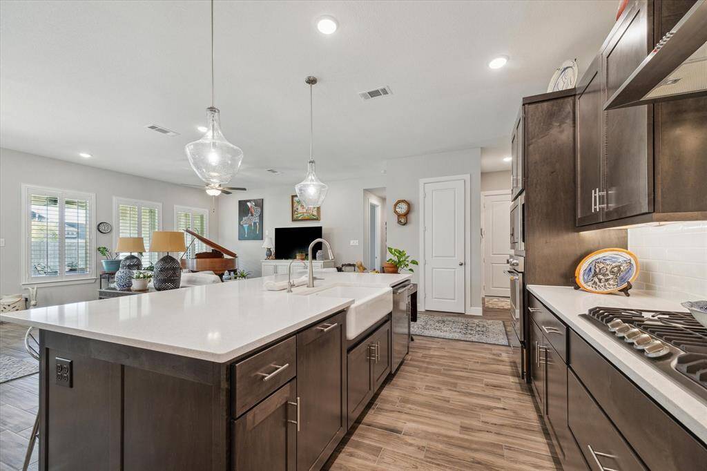 The spacious kitchen opens to the living area, featuring a large island with quartz countertops, a farmhouse sink, and pendant lighting. Ideal for entertaining and family gatherings. This view showcases the seamless flow of the living, dining, and kitchen area.  The kitchen also features a large pantry (7.8 x 4.8), providing abundant storage space.